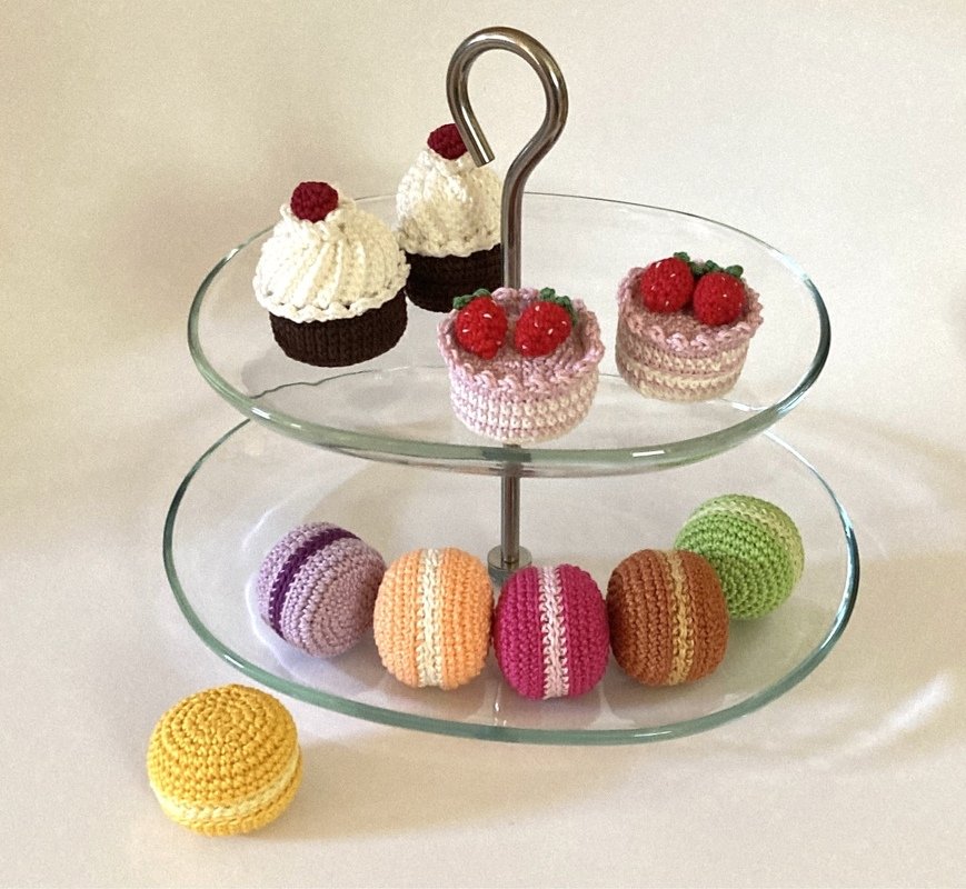 Gehäkelte Süßigkeiten auf einer Etagere: Cupcakes, kleine Törtchen und bunte Makronen.