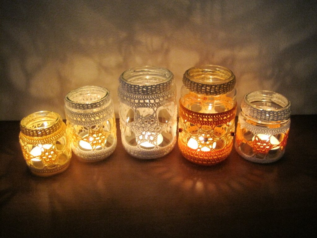 Einmachgläser mit gehäkelten Spitzenmanschetten und brennenden Teelichtern