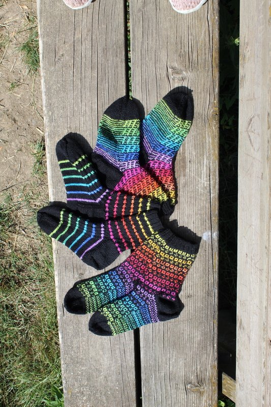 Black-based knitted socks with colorful rainbow stripe and mosaic patterns laid on a wooden bench.