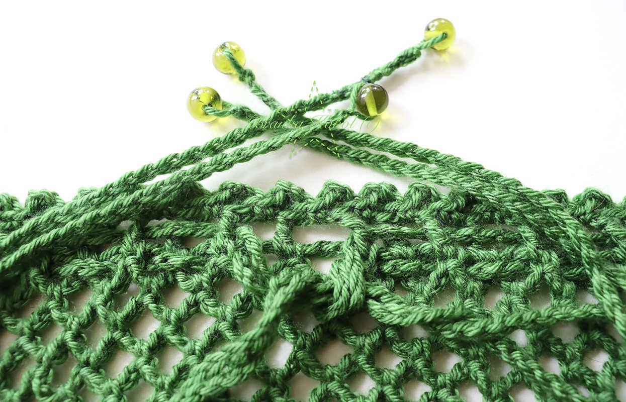 Nahaufnahme eines grünen Häkelnetzes mit offenem Maschenmuster und gelb-grünen Perlen an der oberen Kordel.