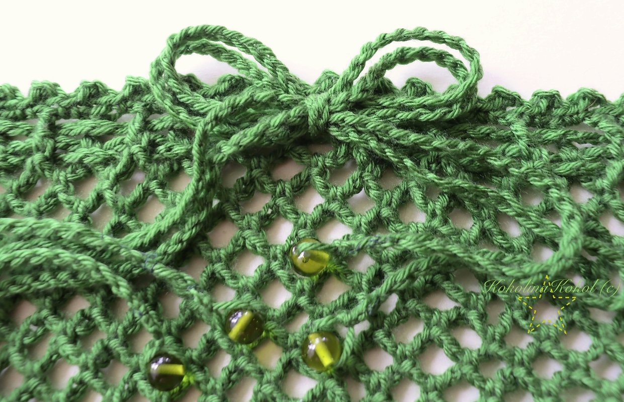 Nahaufnahme eines grünen gehäkelten Netzes mit Perlen und Garnschleife