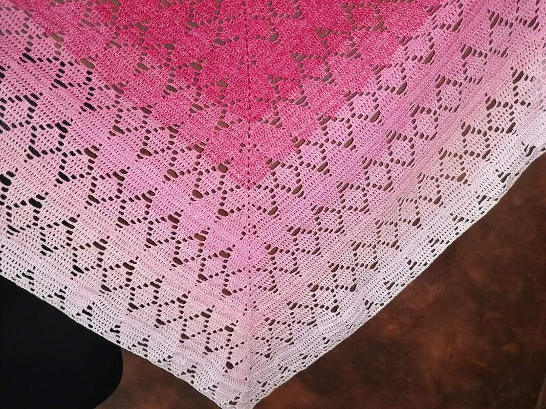 Gehäkeltes Dreieckstuch mit Lochspitzenmuster und Farbverlauf von Pink zu Weiß auf dunklem Untergrund