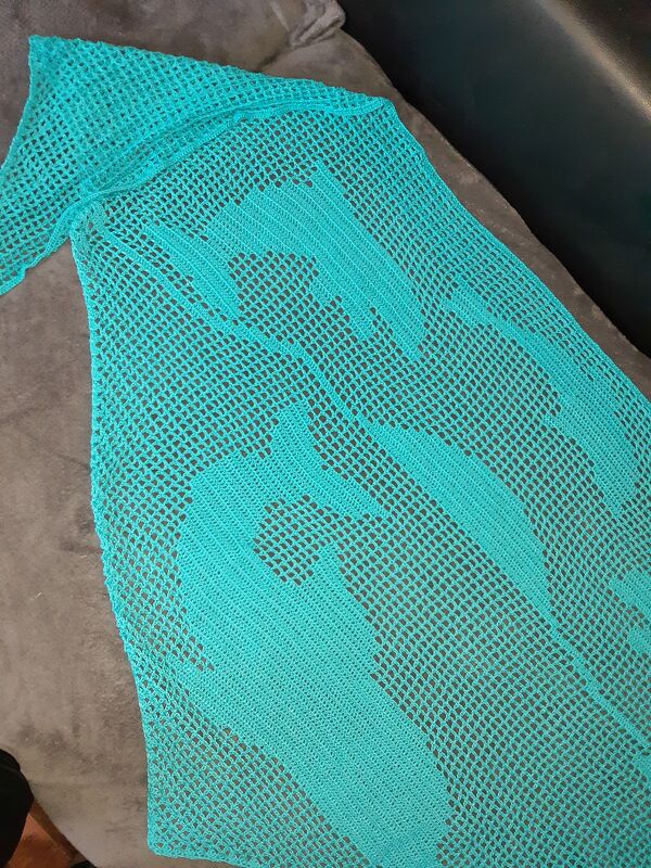 Türkises gehäkeltes Tuch mit offenem Netz und angedeuteten Fischmotiven auf dunklem Untergrund