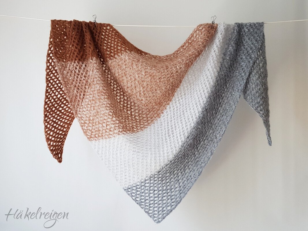 Crocheted triangle shawl in brown, beige, white and grey gradient hanging on a line