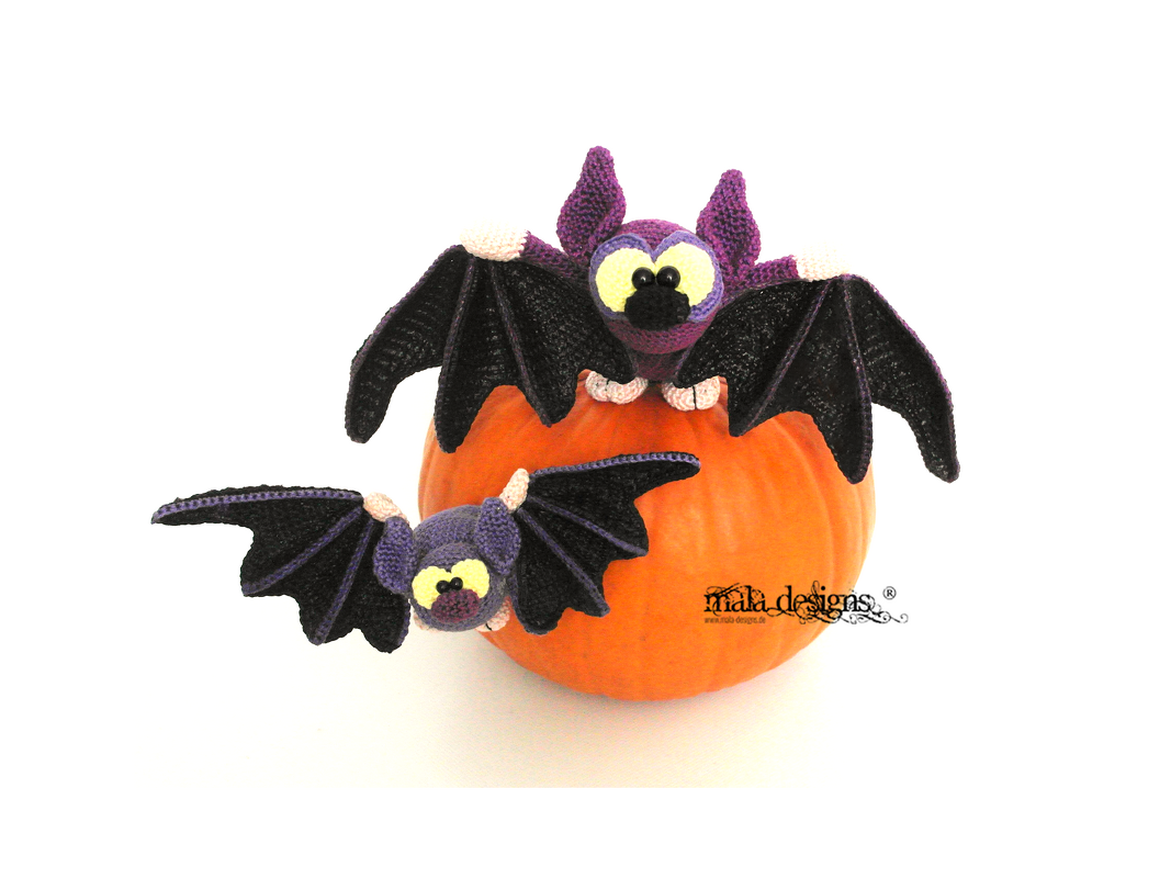 Zwei gehäkelte lila-schwarze Amigurumi-Fledermäuse mit gelben Augen auf einem orangefarbenen Kürbis