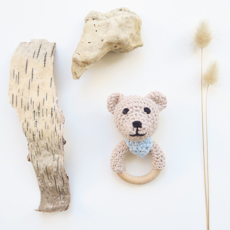 Gehäkelter Bärenkopf mit hellblauem Halstuch an rundem Holzgreifring auf weißem Hintergrund