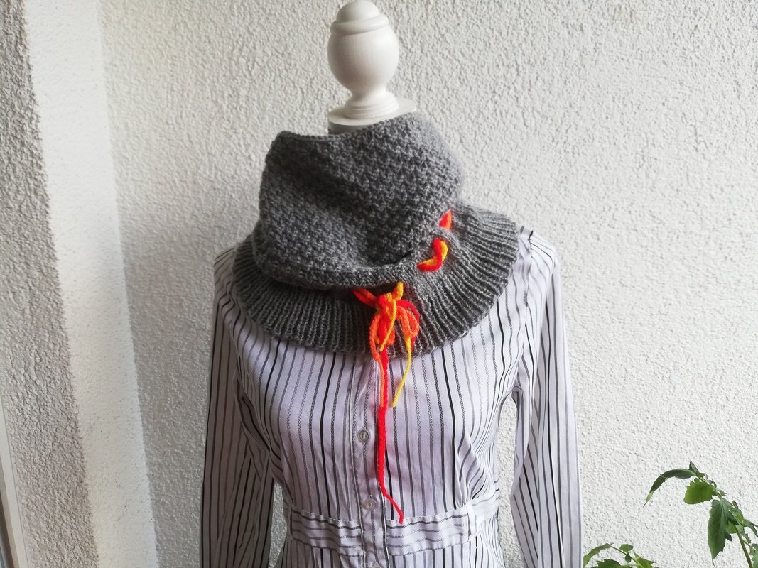 Detailaufnahme eines grauen Loops mit Rippenbund und orange-gelber Schnürung