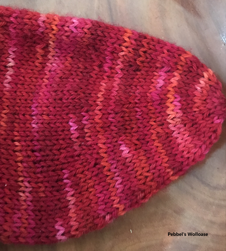Gestrickte Sockenspitze in Rot-, Orange- und Pinktönen mit meliertem Streifenmuster auf Holzuntergrund.