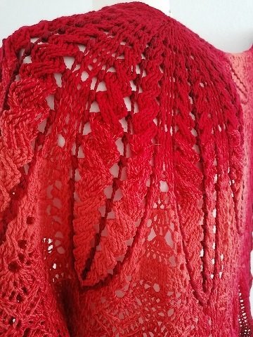 Nahaufnahme eines gehäkelten Halbrundtuchs in Rot-Orange mit sichtbarem Lochmuster und Farbverlauf.