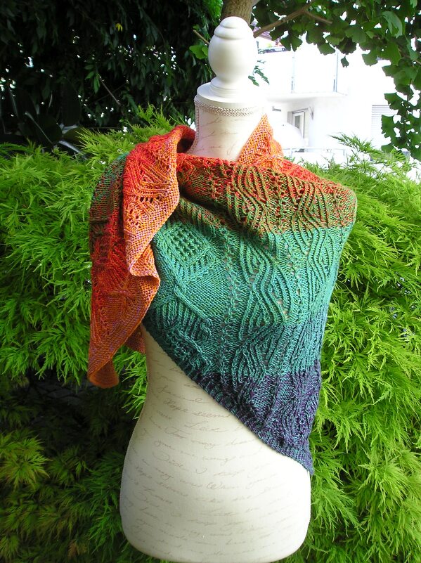 Handgestricktes Dreieckstuch mit Zopf-, Loch- und Rippenmustern sowie Ombré-Farbverlauf auf einer Büste