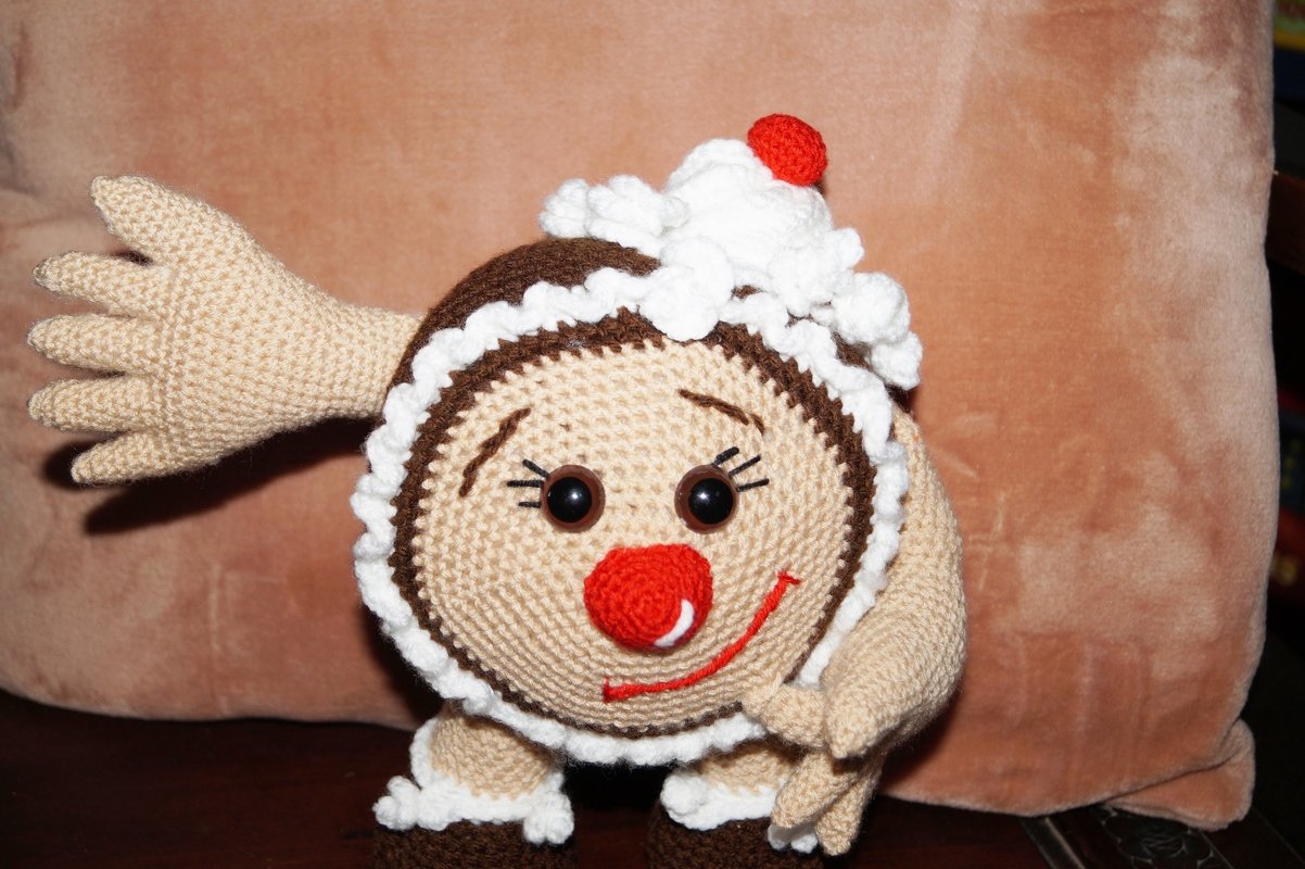 Gehäkeltes Lebkuchen-Amigurumi mit Zuckerguss-Details und roter Kirsche auf hellem Hintergrund.