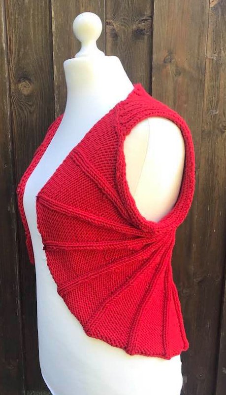 Rote Strickweste mit f
00E4cherf
0006rmigem Muster auf wei
00DFer Schneiderpuppe vor Holzlattenzaun.