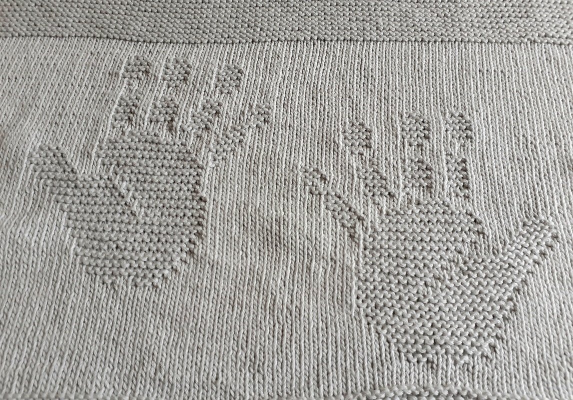 Hellgraue gestrickte Decke mit zwei eingestrickten Handmotiven