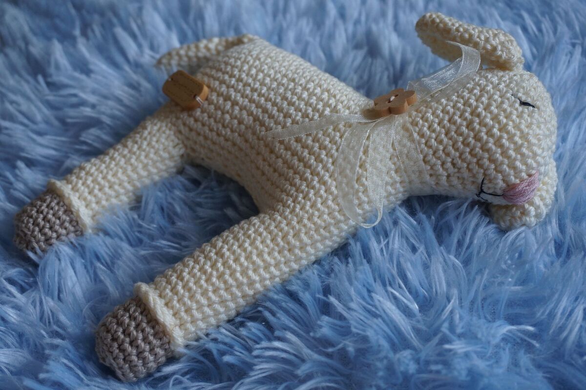 Handgehäkeltes Amigurumi-Lamm in Creme mit Holzknöpfen und Band auf blauem Flausch.