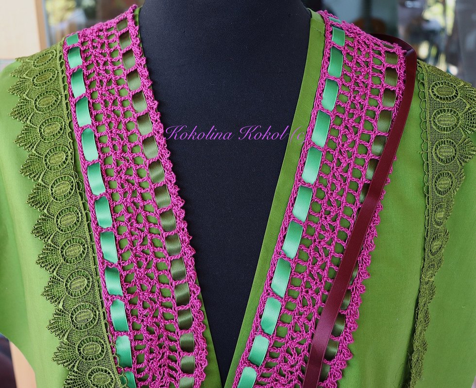 Grüne Bluse mit pinker Häkelborte und grünem Satinband am V‑Ausschnitt auf Schneiderbüste