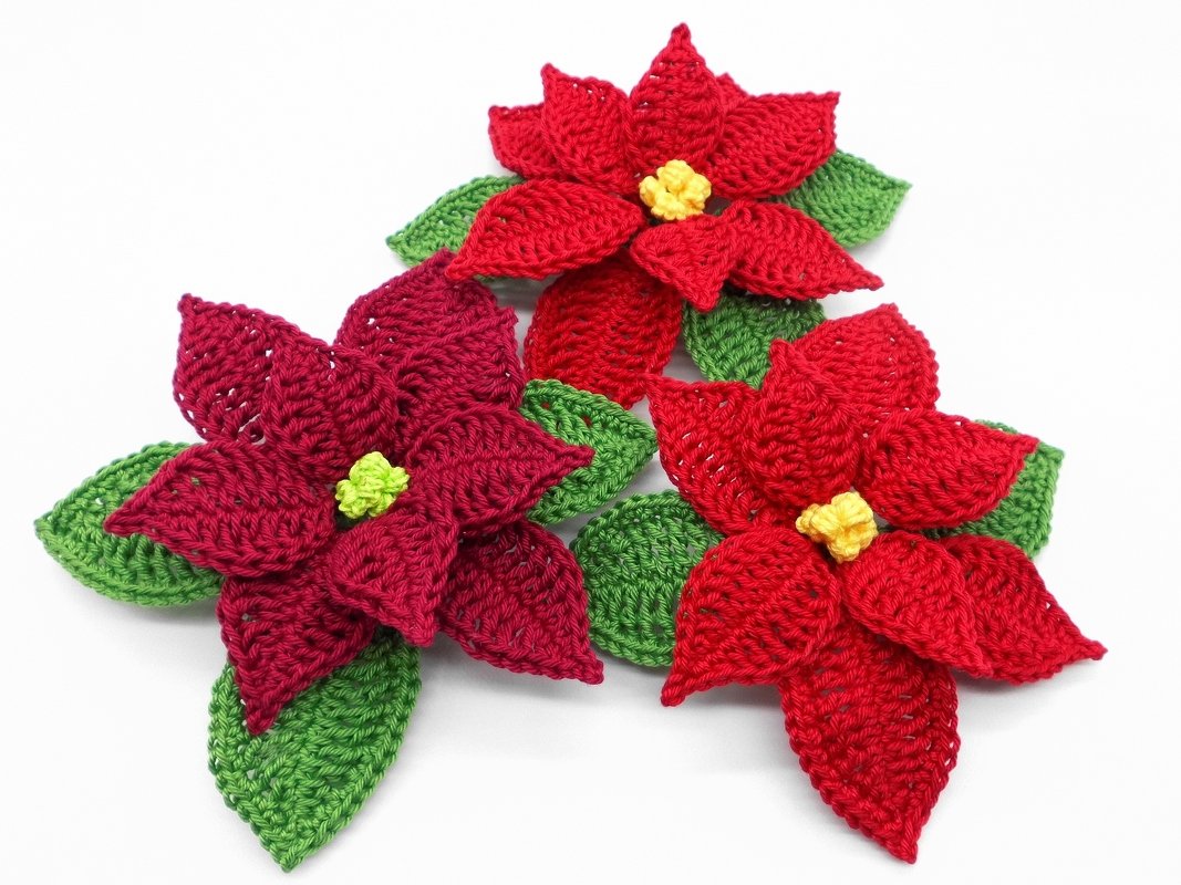 Detailansicht von drei gehäkelten Weihnachtssternen mit sichtbaren Maschen und grünen Blättern