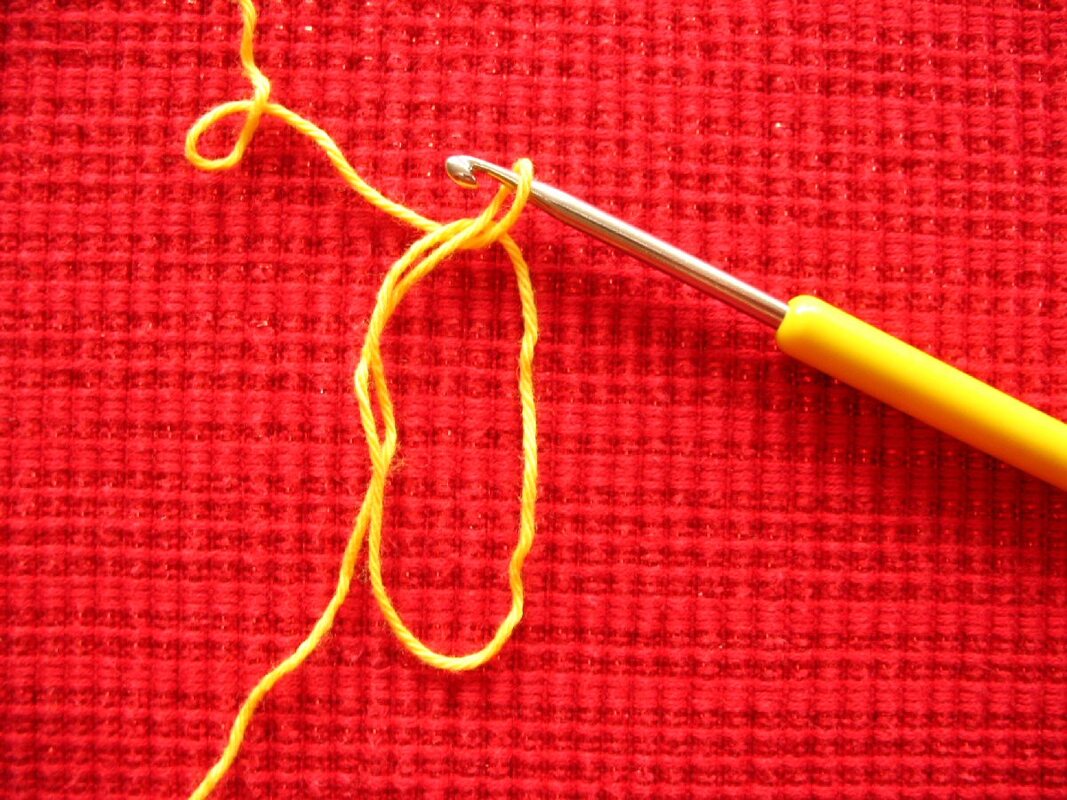 Gelbe Häkelnadel mit gelbem Garn auf rotem Stoff