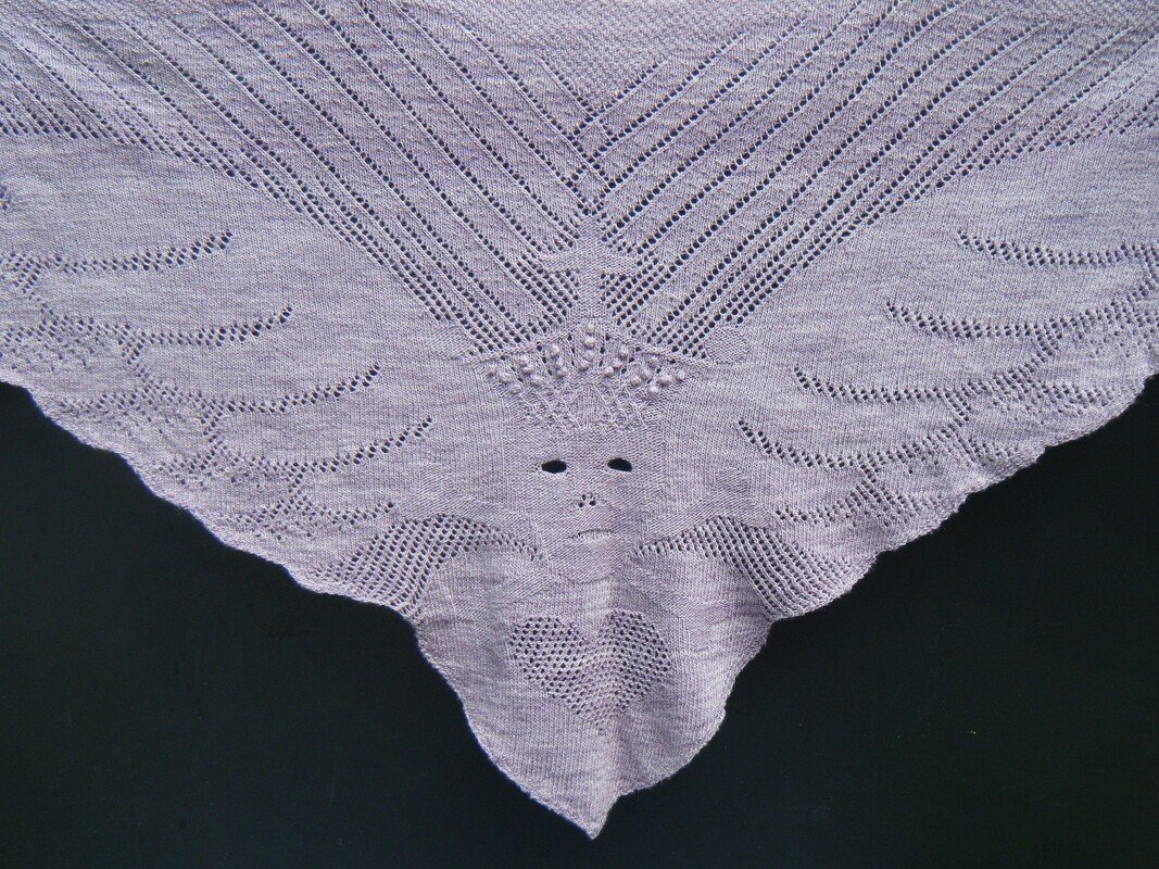 Light purple triangular lace shawl with a stylized face and heart motif on a dark background.
