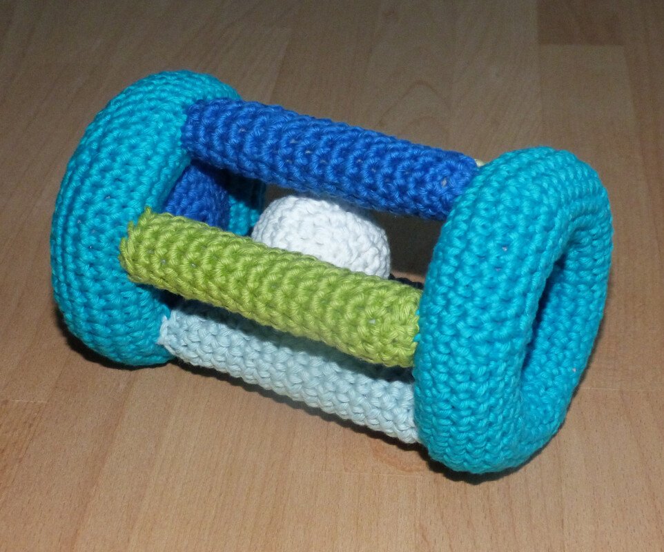 gehäkelter Baby-Greifling mit türkisen Ringen und bunten Stäben auf Holzboden