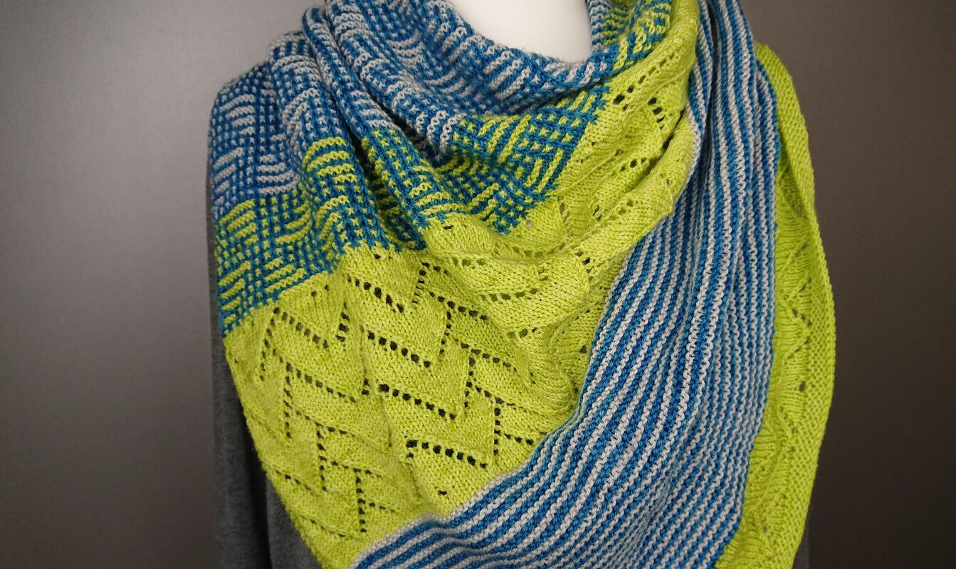 Knitted triangle shawl in blue, white, and lime green showing mosaic, chevron lace, and striped sections