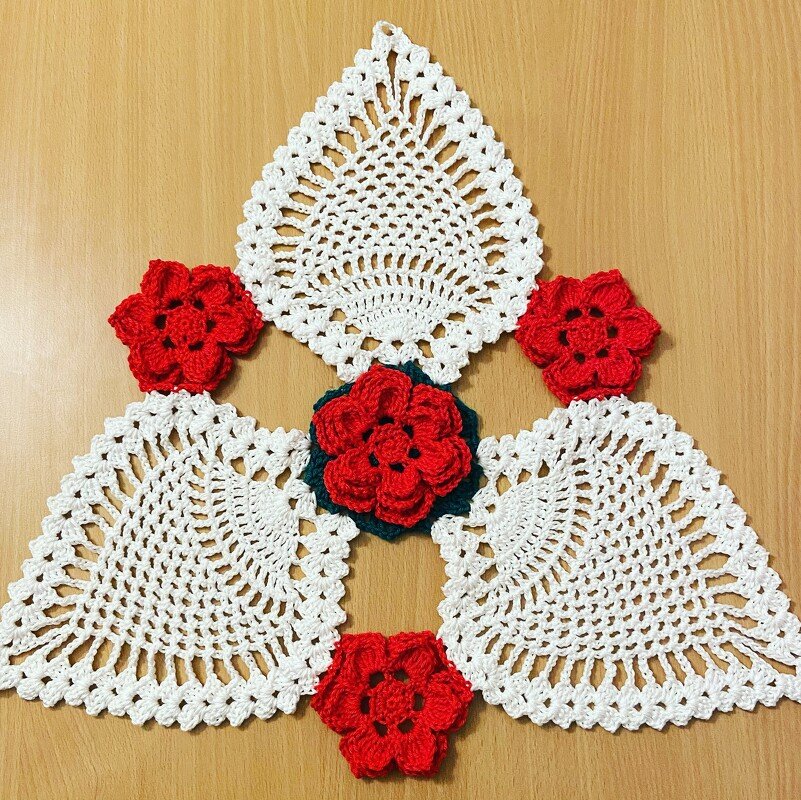 Weiße gehäkelte Deckchen und rote Häkelblumen auf Holzoberfläche