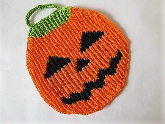 Gehäkelter orangefarbener Topflappen in Kürbisform mit schwarzem Jack-o'-Lantern-Gesicht und grüner Schlaufe