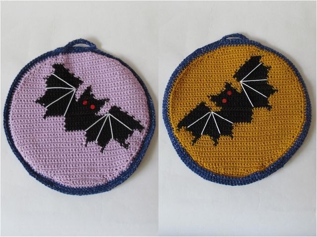Zwei runde gehäkelte Topflappen: links lila mit schwarzer Fledermaus, rechts senfgelb mit schwarzer Fledermaus, beide mit blauem Rand und Aufhängeschlaufe.