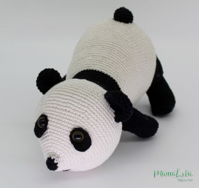 Gehäkelter Panda‑Amigurumi liegend mit schwarzem Kopf‑ und Beinbesatz