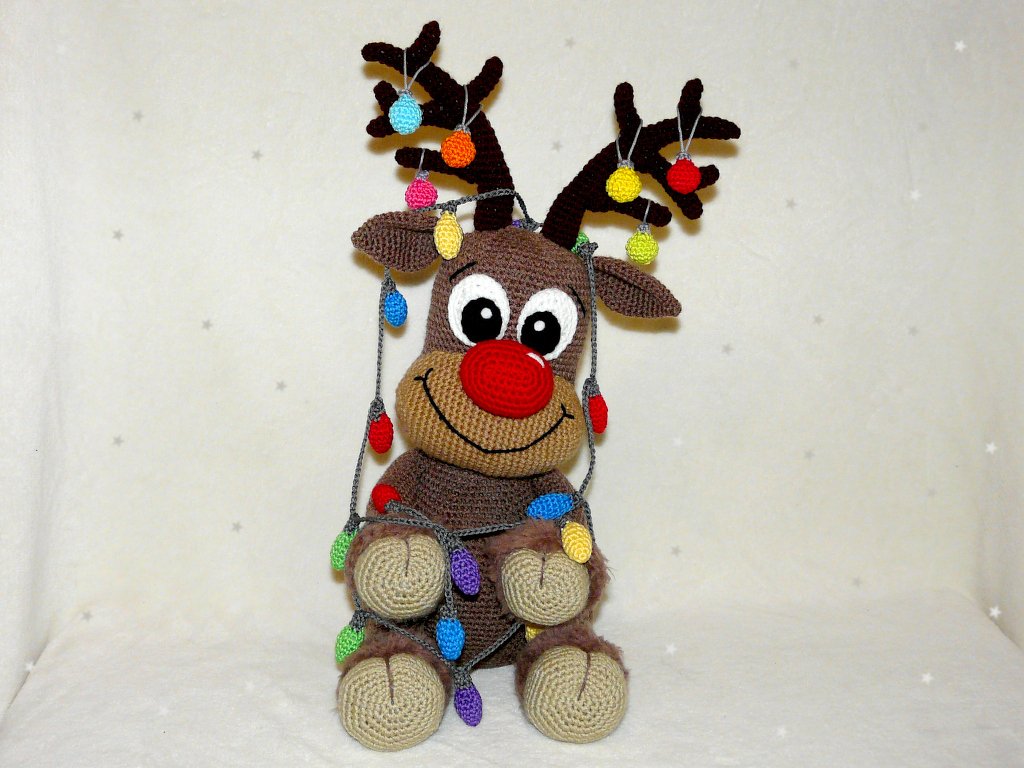 Brown crocheted reindeer amigurumi with a red nose and multicolored crocheted lights wrapped around its antlers and body.