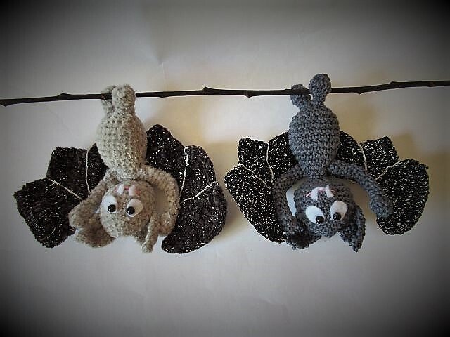 Zwei gehäkelte Fledermäuse (hellgrau und dunkelgrau) hängen kopfüber an einem Ast