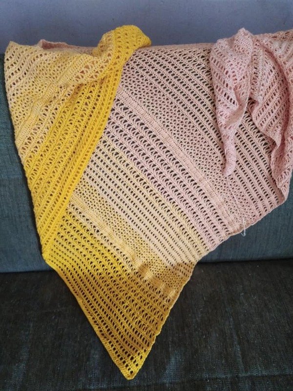 Handgehäkeltes Dreieckstuch in Gelb und Rosa mit Lochmuster auf dunkelblauer Sofalehne