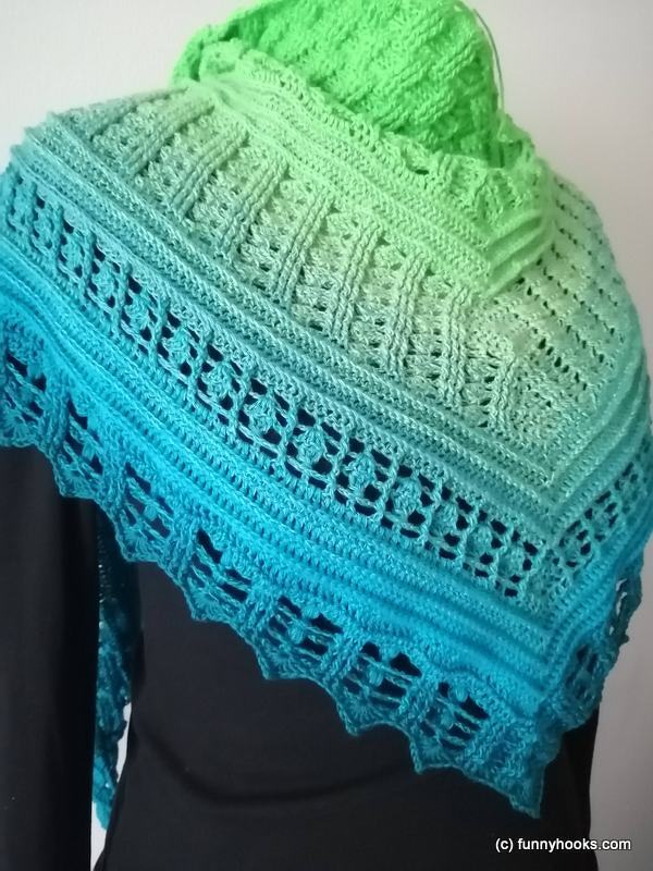 Crochet triangle shawl in green to blue ombre with textured stitches, openwork lace, and scalloped edge.