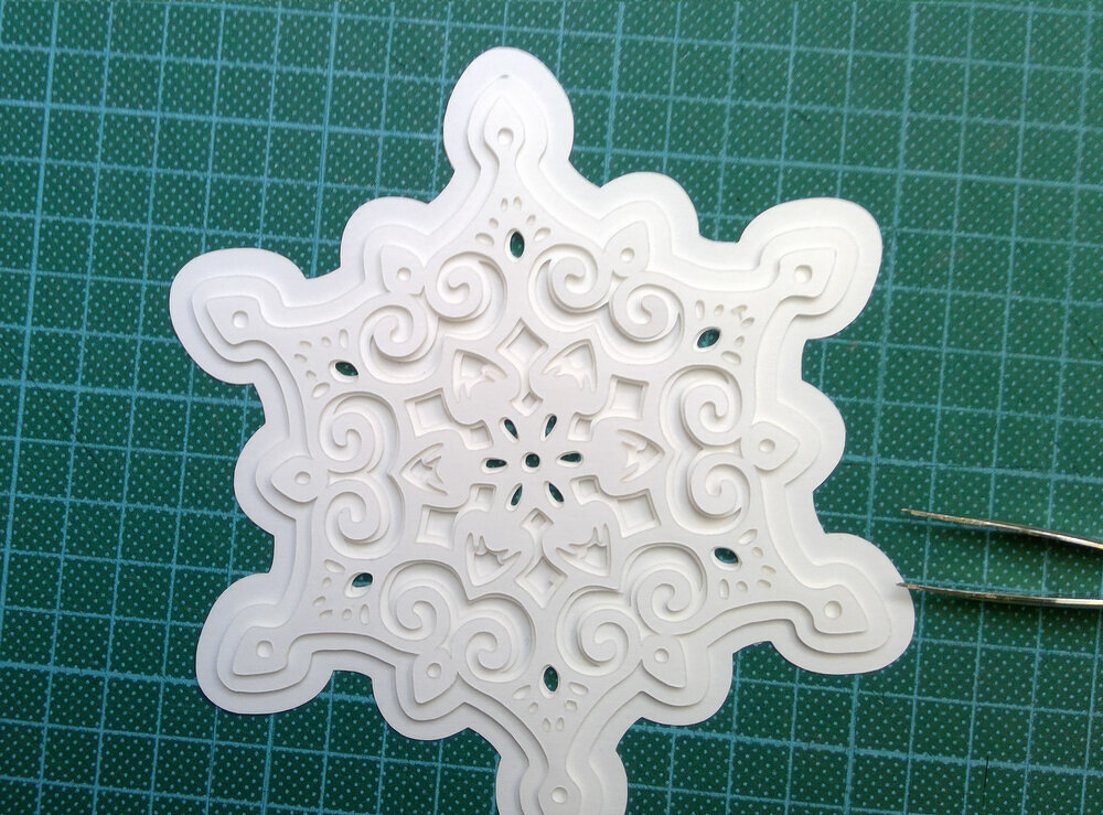 Weißes mehrlagiges Schneeflockenmotiv auf grüner Schneidematte