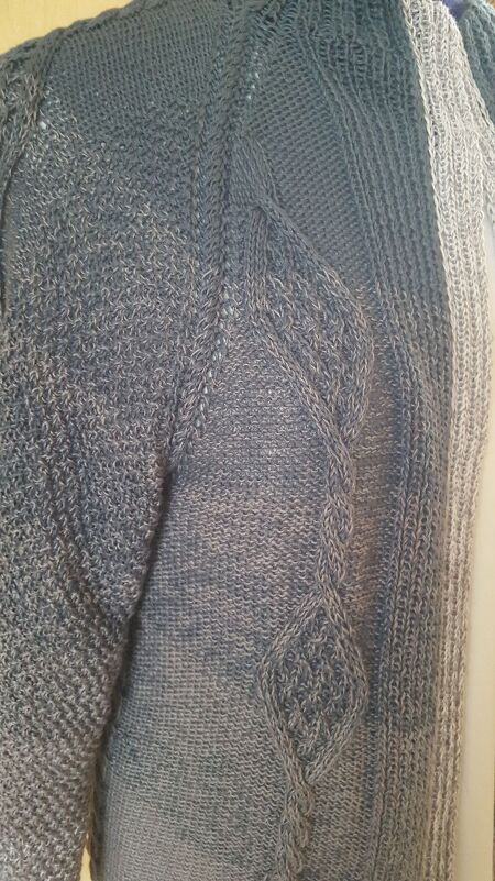 Nahaufnahme einer grauen Damenstrickjacke mit seitlichem Zopfmuster und Blattmotiven