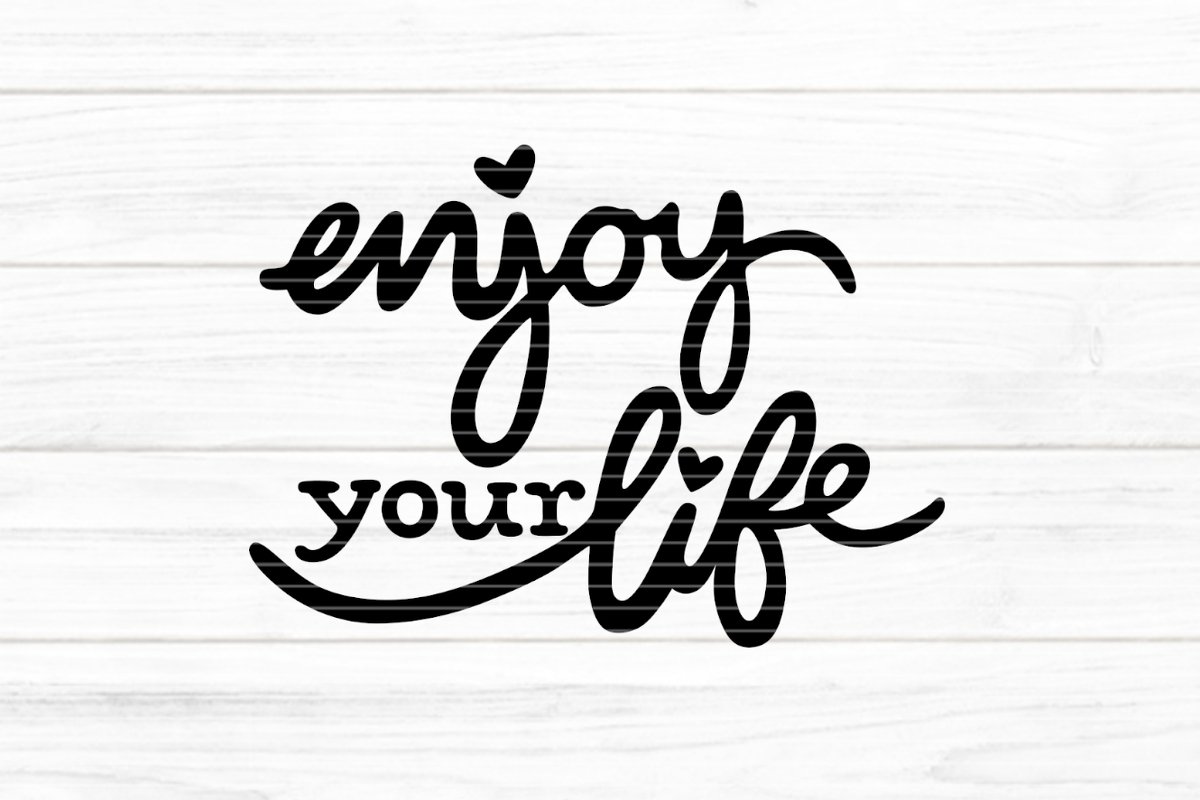Schwarzer Script‑Schriftzug „enjoy your life“ mit Herz‑Details auf hellem Holzuntergrund
