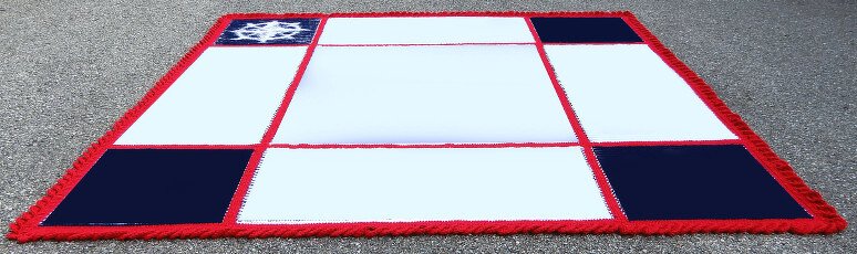 Gestrickte Decke mit weißen und dunkelblauen Quadraten, rotem Rand und Fransen