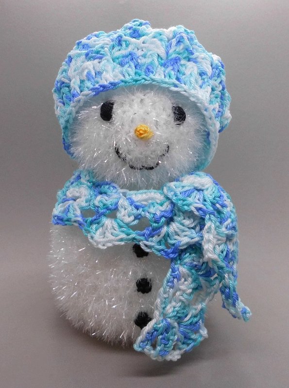 Gehäkelter weißer Schneemann mit blau-weißer Mütze und Schal vor neutralem Hintergrund.