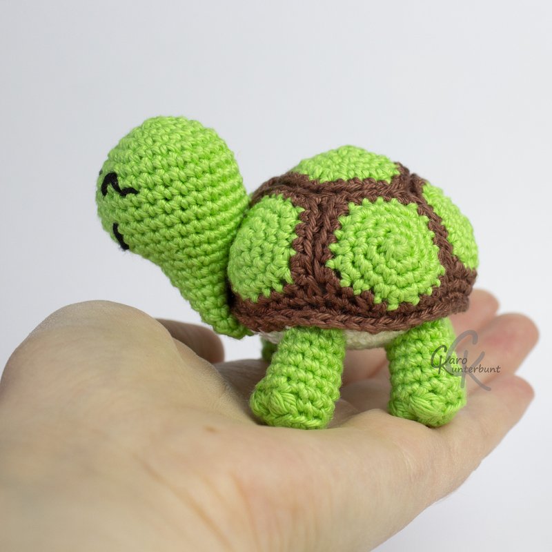 Hand hält kleine gehäkelte Schildkröte aus grünem und braunem Garn