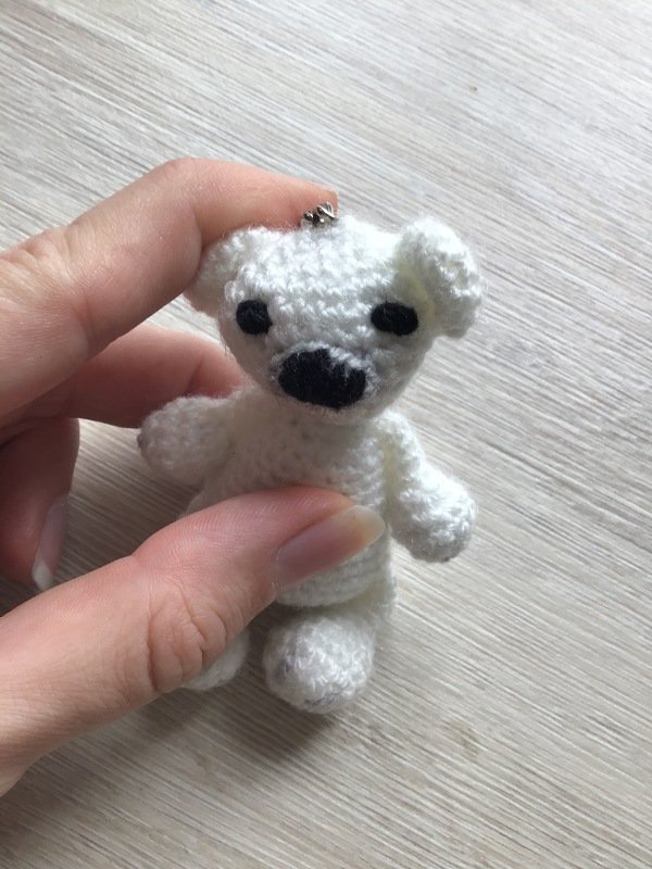 Hand hält kleinen weißen gehäkelten Amigurumi-Bären mit Metallöse