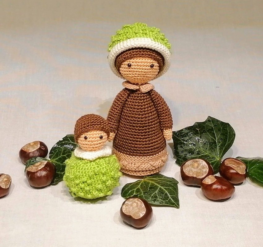 Zwei gehäkelte Amigurumi-Puppen in Braun und Grün, dekoriert mit Kastanien und Efeublättern