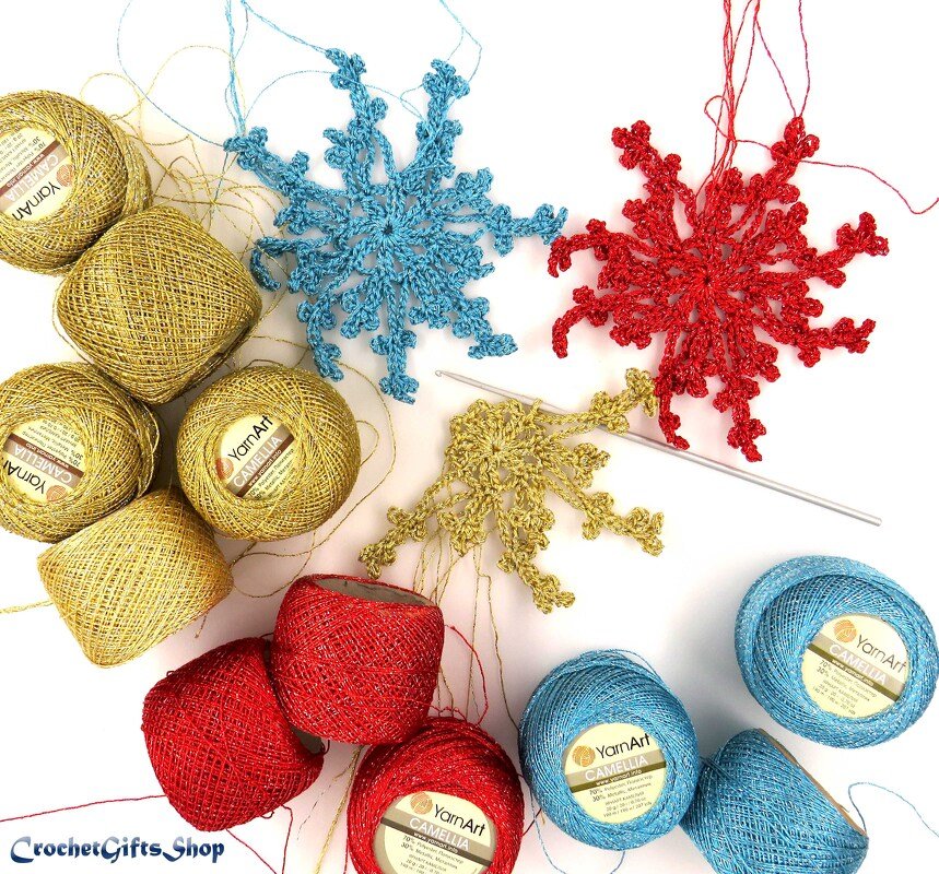 Gold, red, and blue metallic crochet snowflake ornaments with matching thread balls and a crochet hook on a white background