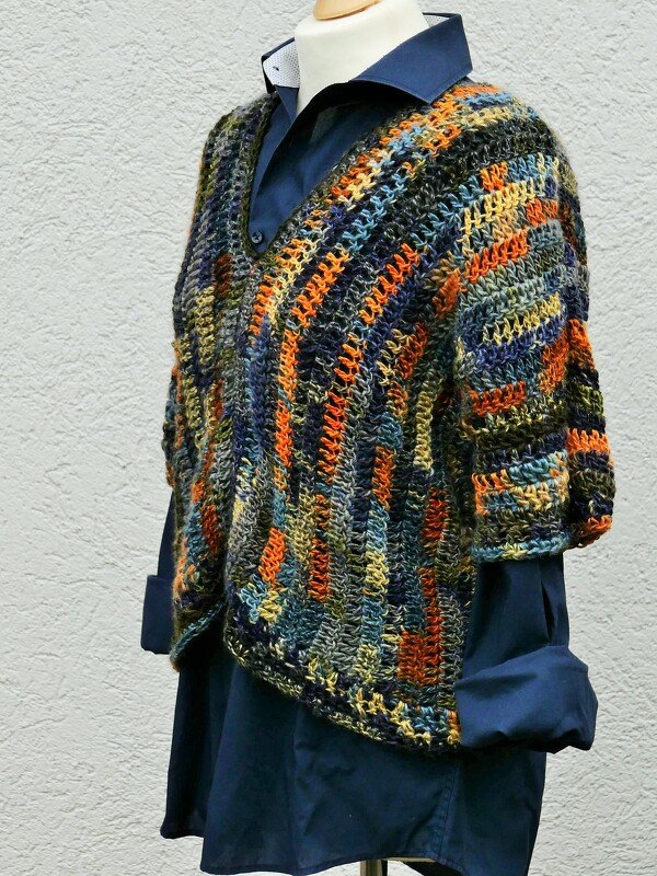 Gehäkelter Damen-Poncho in Orange, Blau und Grün mit V-Ausschnitt auf einer Schaufensterpuppe über einem dunkelblauen Hemd.