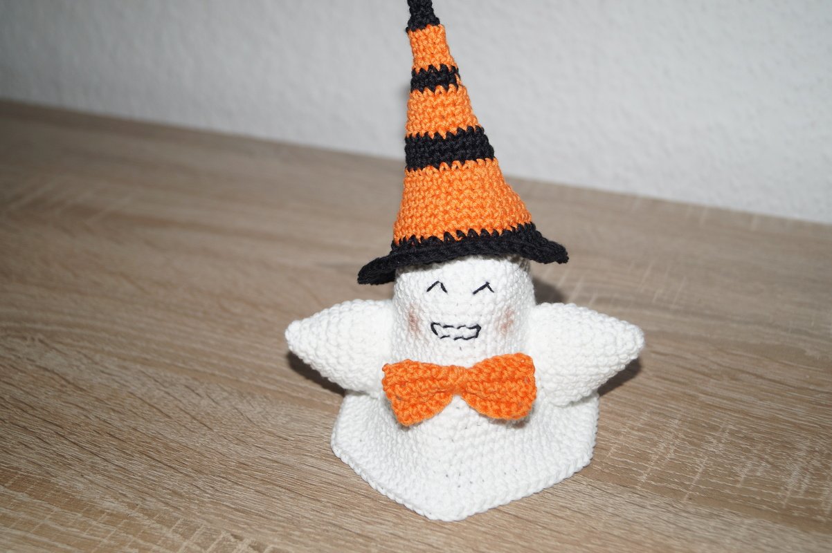Kleines weißes Häkelgespenst mit gestreiftem orange-schwarzem Hut und oranger Schleife