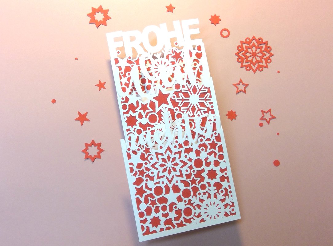 Zweilagige Plottkarte mit ausgeschnittener „Frohe Weihnachten“-Schrift, weißen Schneeflocken und rotem Hintergrund