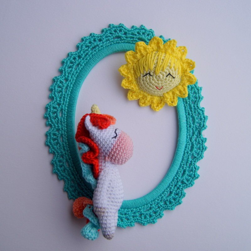 Kleines gehäkeltes Einhorn im ovalen türkisfarbenen Häkelrahmen mit gelber Sonne