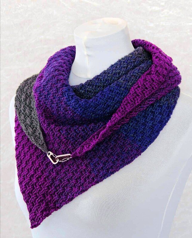 Triangle crochet shawl in purple, blue and gray gradient fastened with a metal pin on a mannequin
