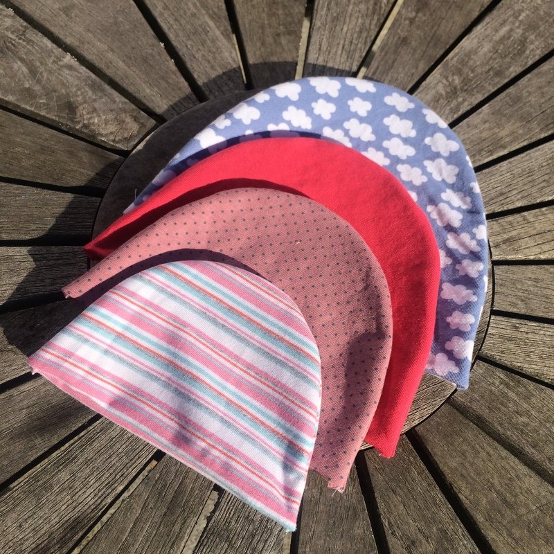 Fächerförmig angeordnete Stoffzuschnitte für Babymützen mit Wolken-, Punkt- und Streifenmustern auf Holz.