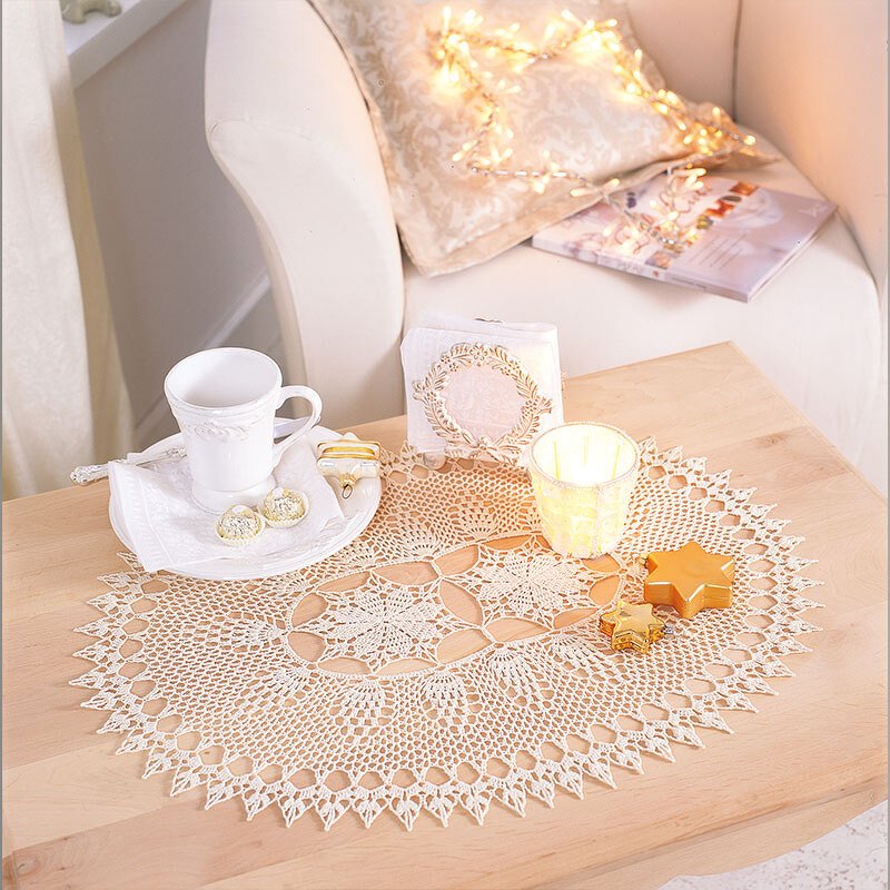 Ovales gehäkeltes Deckchen in Creme auf hellem Holztisch mit Tasse und Kerze