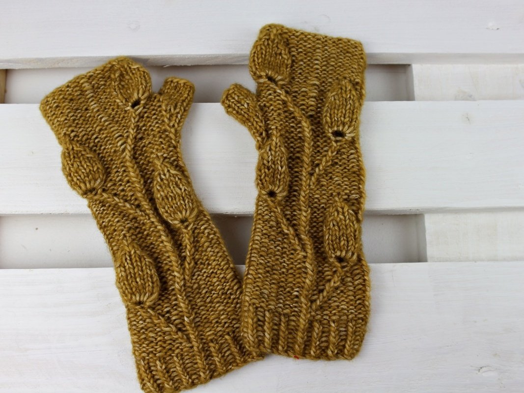 Senfgelbe gestrickte fingerlose Handschuhe mit Blattzopfmuster auf hellem Holz