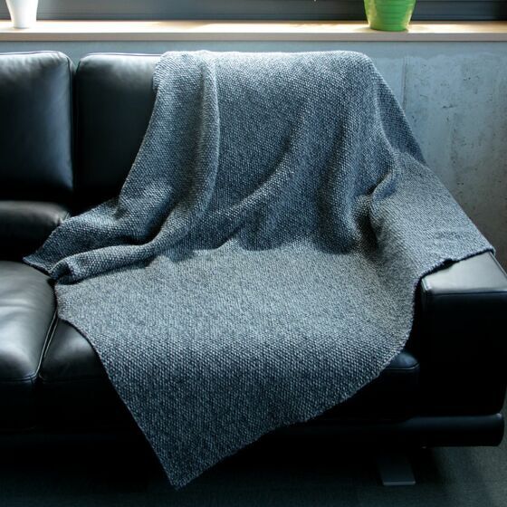 Grau melierte gestrickte Decke über schwarzem Sofa drapiert